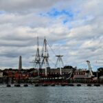 Historic ship docked at a waterfront with monument.