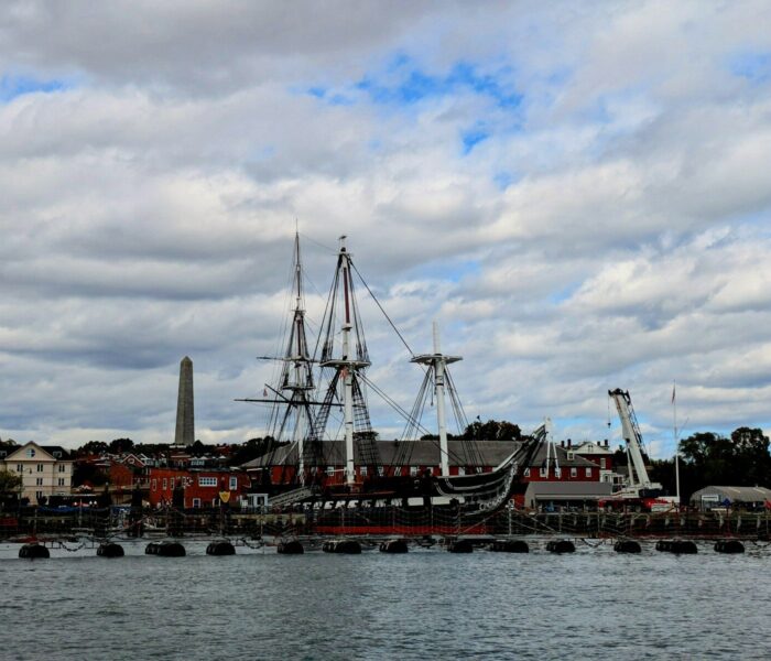 Historic ship docked at a waterfront with monument.